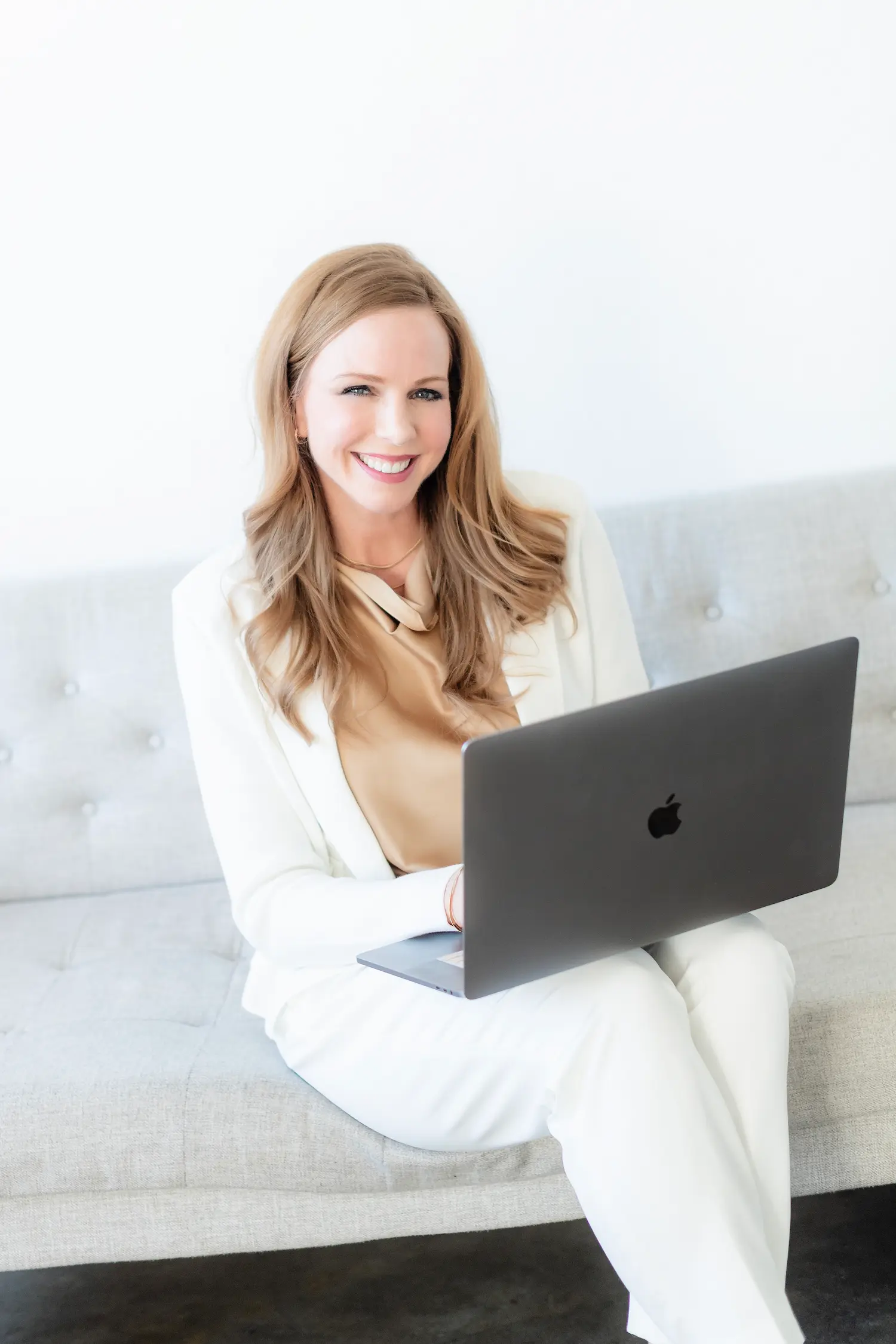 Heather in a white suit, sitting on a couch and working on web compliance on her computer